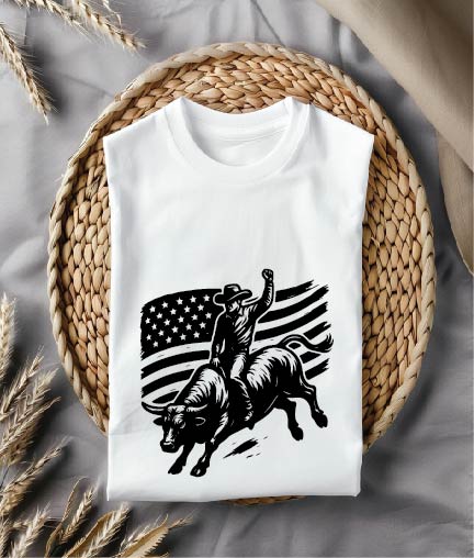 White t-shirt with a graphic design of a cowboy on a bull and an American flag, placed on a woven mat.