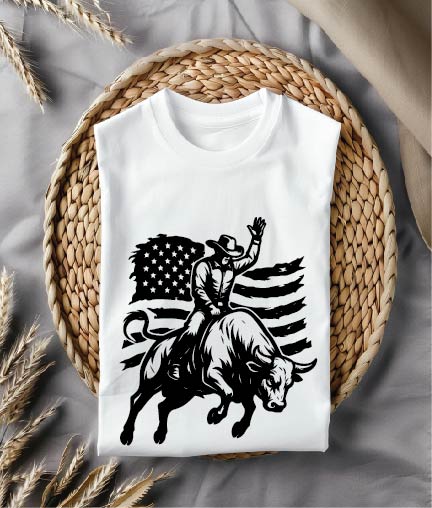 White t-shirt with a graphic of a cowboy riding a bull and an American flag on a woven mat.